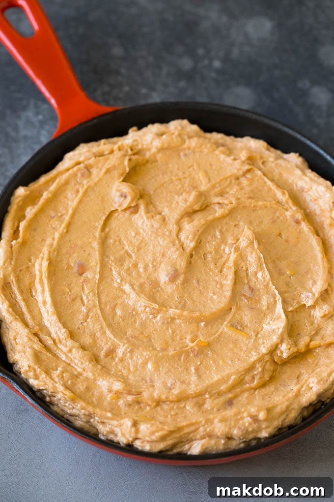 Bean Dip Recipe | Mexican Dip #dip #appetizer #mexicanfood #beans #cheese #dinneratthezoo Creamy refried beans mixed with cream cheese, sour cream, and spices in a mixing bowl, ready for baking.