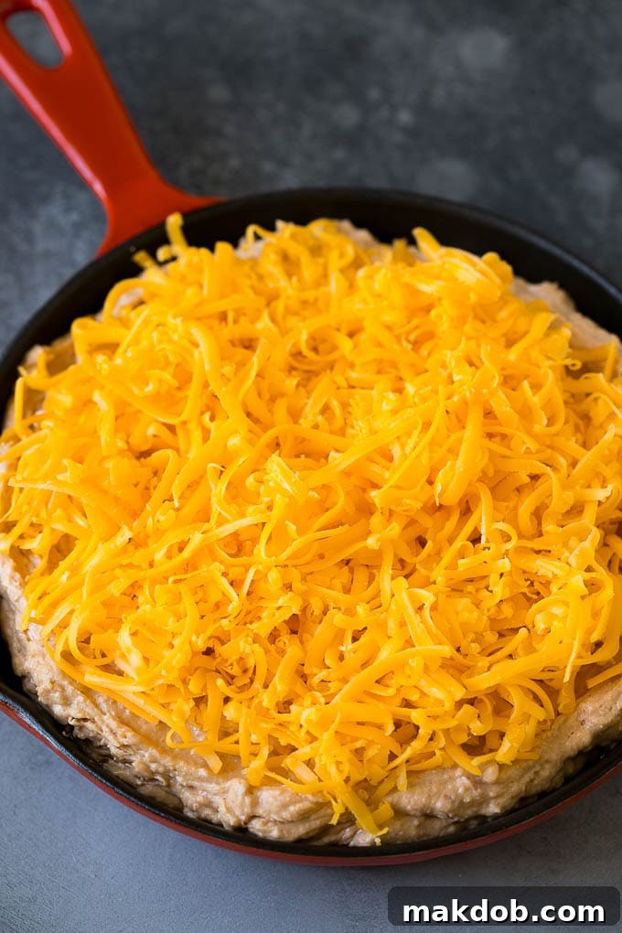 Bean Dip Recipe | Mexican Dip #dip #appetizer #mexicanfood #beans #cheese #dinneratthezoo The bean dip base, smooth and seasoned, covered with a fresh layer of shredded cheddar cheese, ready for baking.