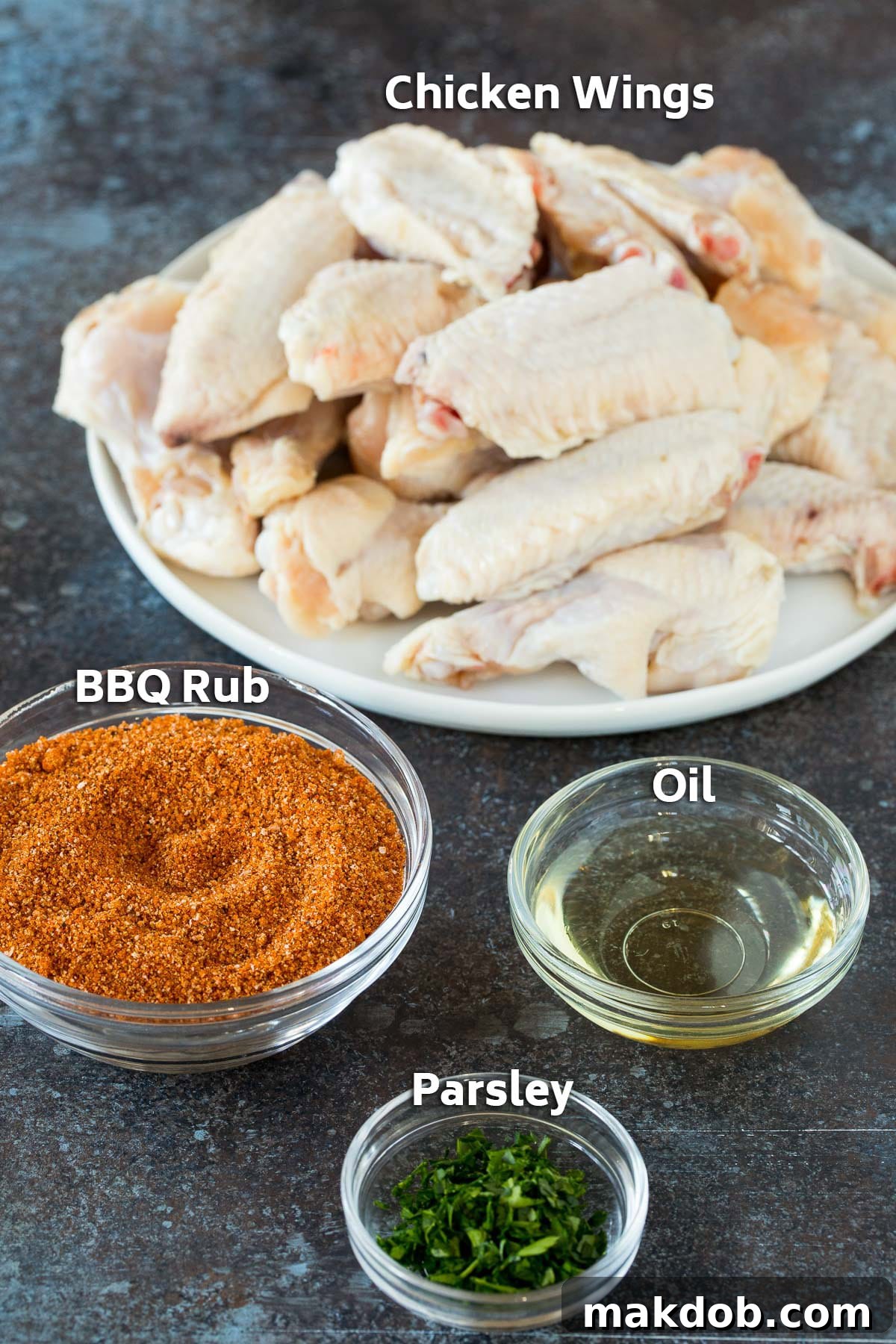 Crispy Oven Wings 3 A plate of raw chicken and bowls of BBQ spice, parsley and oil.