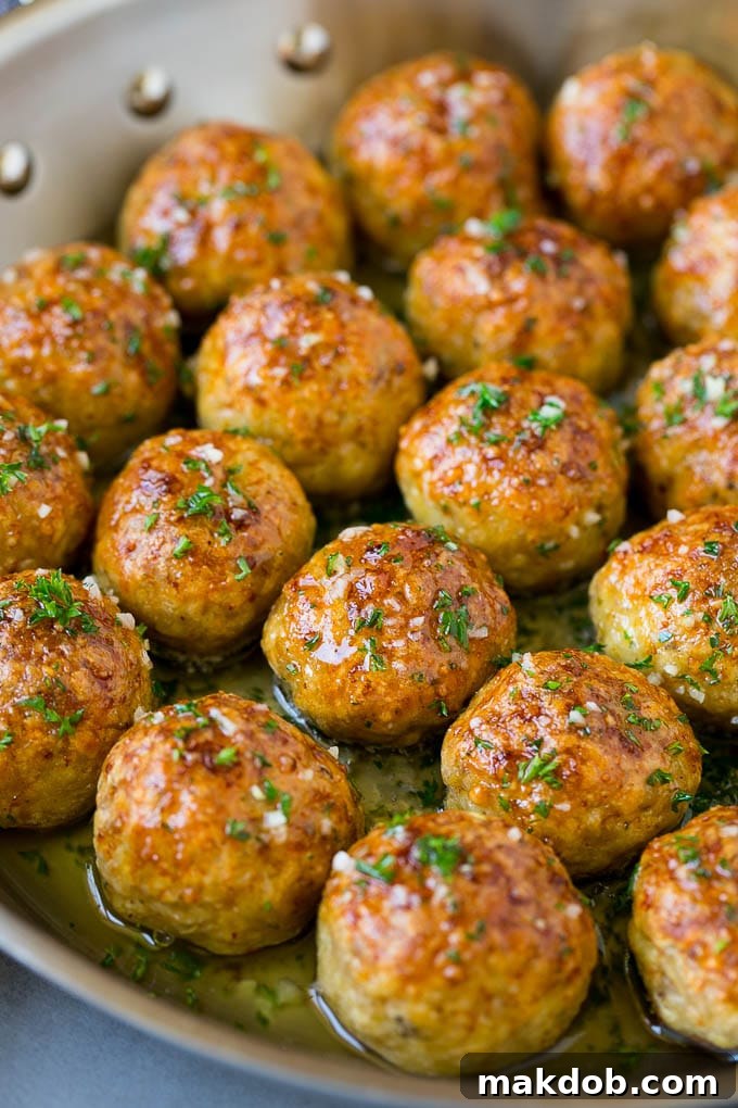 Golden brown chicken meatballs glistening in a skillet with garlic butter sauce, freshly baked and ready to be served.