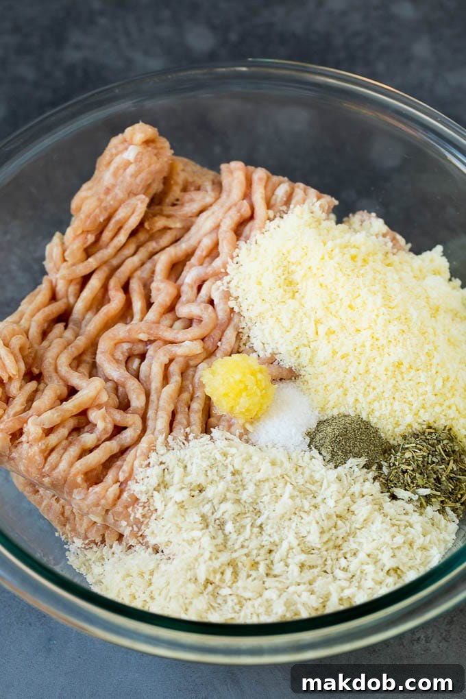 A large mixing bowl containing ground chicken, panko breadcrumbs, grated Parmesan cheese, minced garlic, herbs, and spices, all ready to be combined for homemade chicken meatballs.