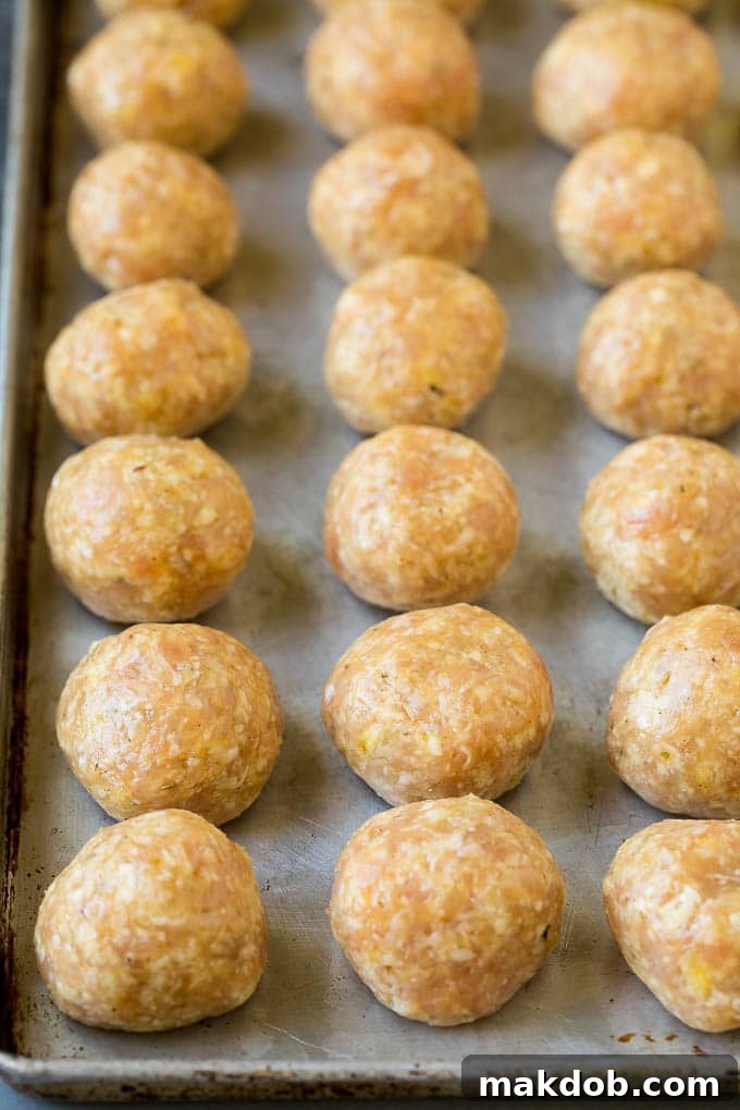 Raw ground chicken mixture with fresh herbs and spices, perfectly rolled into uniform balls on a parchment-lined baking sheet, ready for the oven.