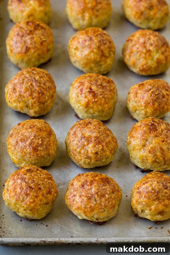 A baking sheet filled with perfectly baked, golden-brown chicken meatballs, fresh out of the oven and garnished with fresh parsley.