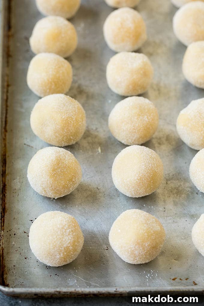 Classic Jam Thumbprint Cookies | Sugar Cookies with Jam Filling #cookies #baking #christmas #dessert #homemade Close-up of perfectly rolled cookie dough balls, coated in granulated sugar, ready for indentation and filling.