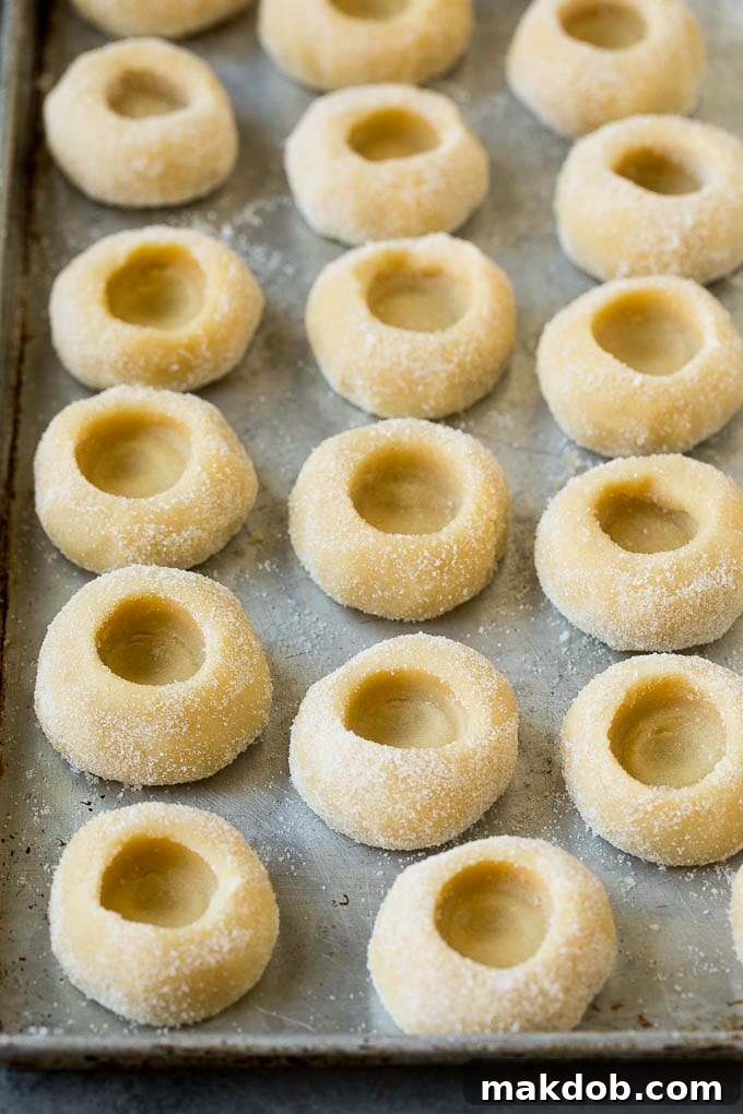 Classic Jam Thumbprint Cookies | Sugar Cookies with Jam Filling #cookies #baking #christmas #dessert #homemade Cookie dough balls on a baking sheet, each with a perfect indentation, ready for their jam filling.