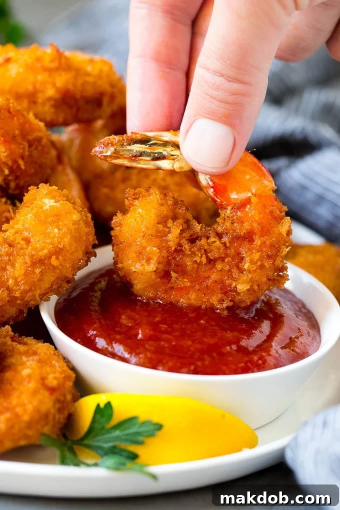 A hand dipping a shrimp into cocktail sauce.
