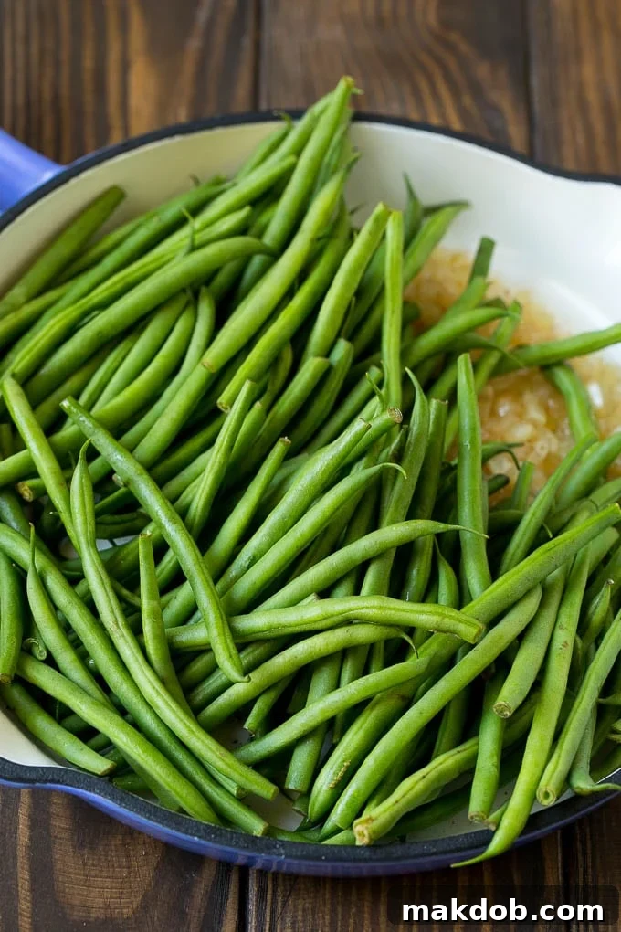 Fresh green beans in a pan with diced onions, ready for cooking.