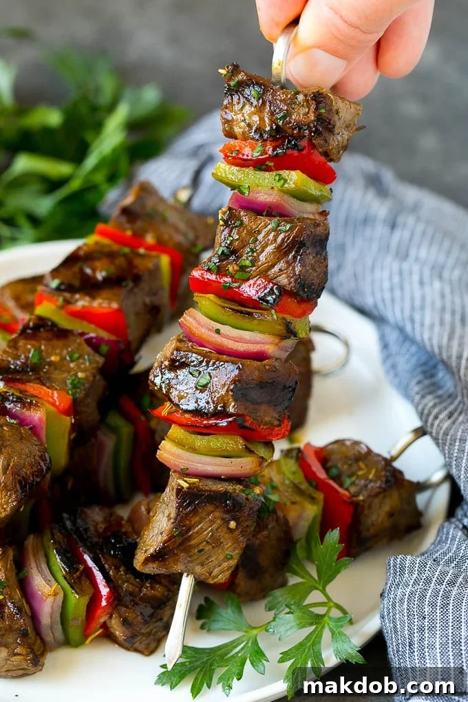 Hand Holding a Perfectly Grilled Beef Shish Kabob A hand holding a beef shish kabob with peppers and onions.