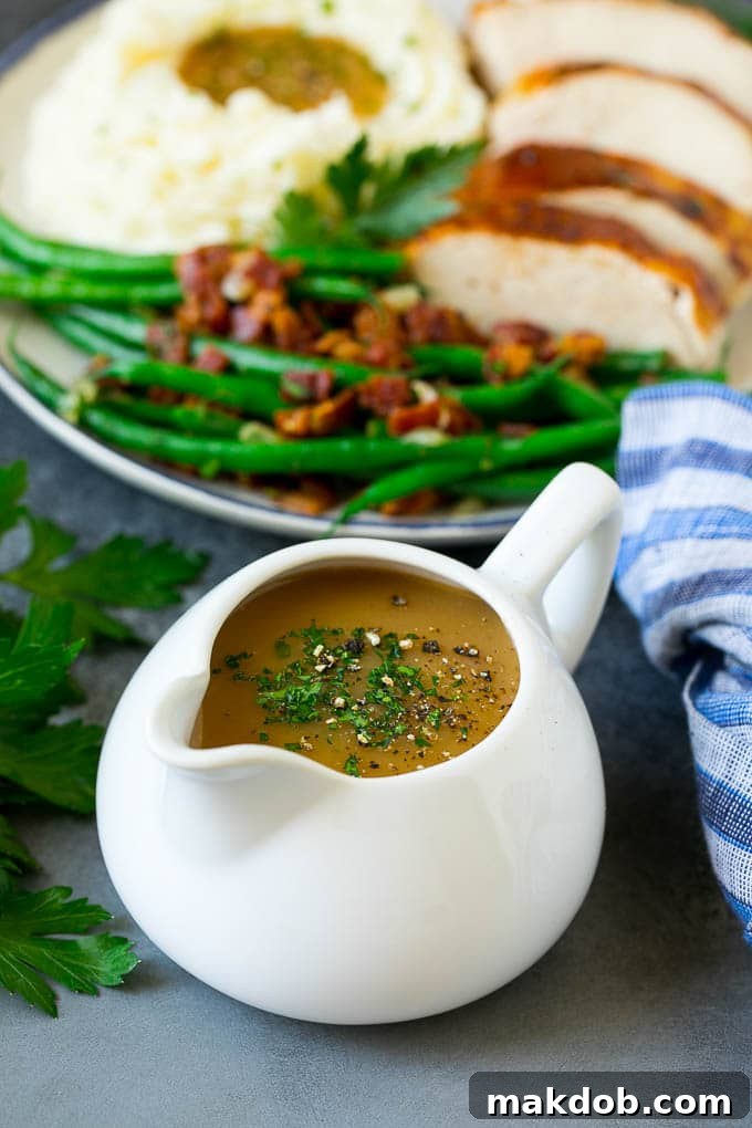 A elegant glass pitcher of perfectly smooth and rich turkey gravy, garnished with fresh parsley sprigs.