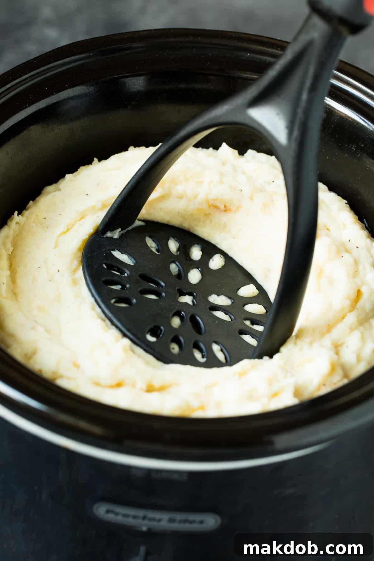 A masher in a slow cooker full of potatoes.