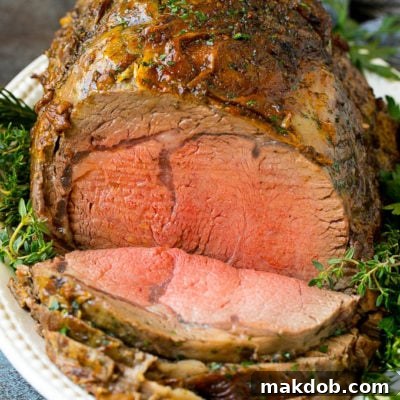 Ultimate Slow Roasted Prime Rib 2 A sliced prime rib roast surrounded by fresh herbs.