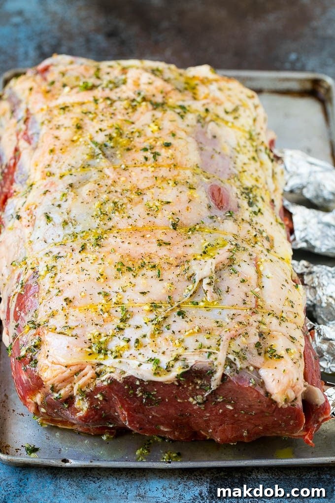 A prime rib roast generously coated with a savory rub of garlic, fresh herbs, and olive oil, glistening and ready for roasting.