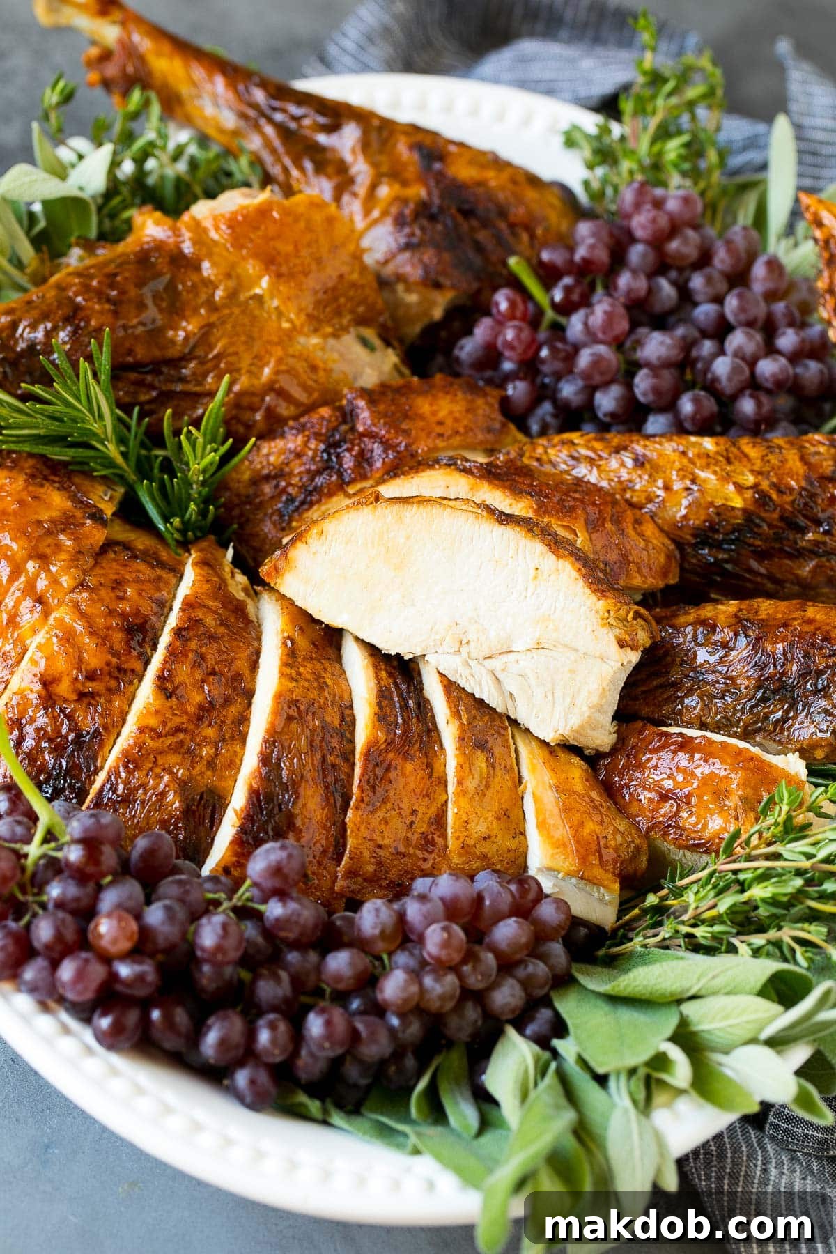 Beautifully sliced deep fried turkey, arranged on a serving platter and garnished with fresh grapes and herbs.