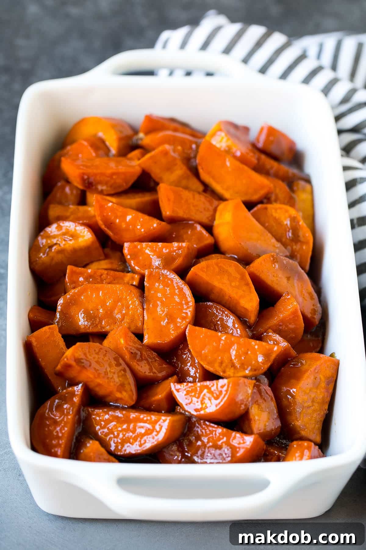 Sweet Potato Candies 5 A close-up shot of a baking dish filled with vibrant yams coated in a glistening sugar sauce, ready for roasting.