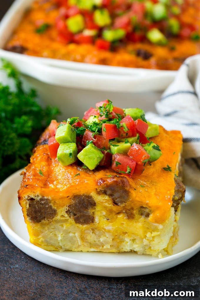 A delectable slice of sausage egg casserole, beautifully garnished with fresh tomatoes and herbs, ready to be served on a white plate.