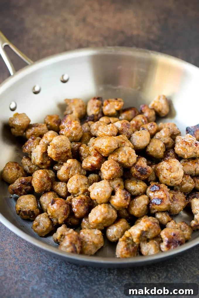 Sizzling breakfast sausage cooking in a cast iron skillet, broken into small, savory pieces.