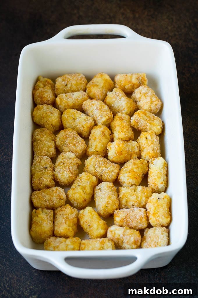 A pristine layer of frozen potato tots covering the bottom of a glass casserole dish, ready for the egg mixture.