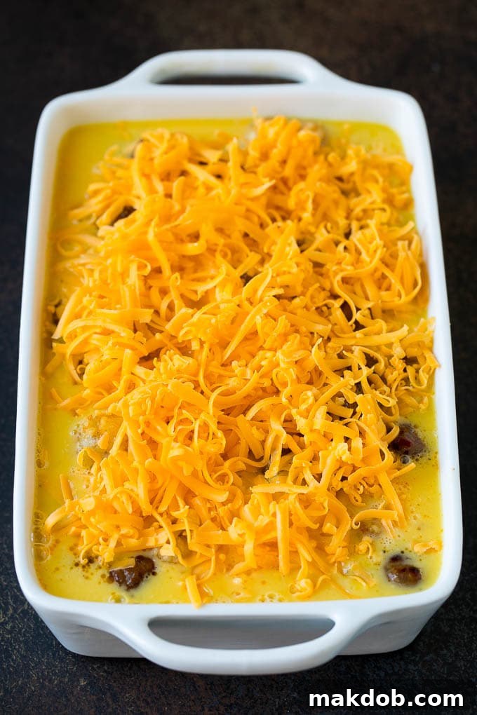 An unbaked sausage egg casserole, layered with potato tots, egg mixture, and cheese, waiting to be placed in the oven.