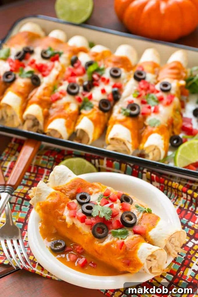A close-up of pumpkin enchiladas on a small plate, perfectly garnished, with a full tray of enchiladas visible in the background.