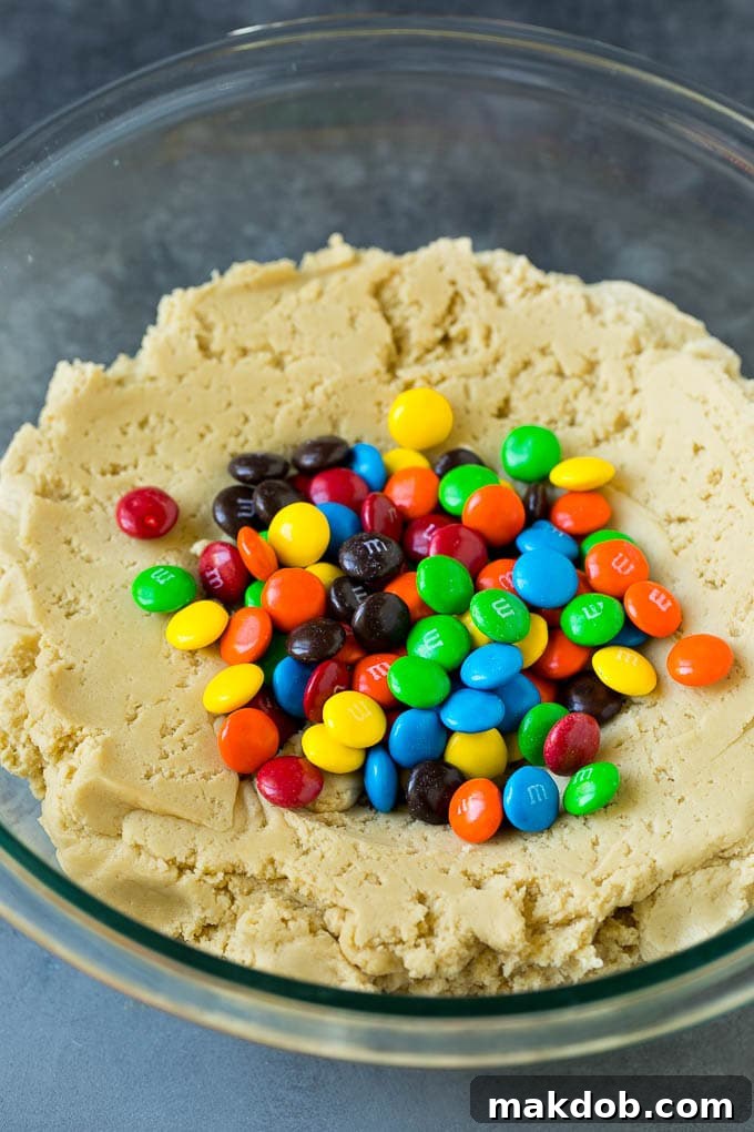 A bowl filled with rich, brown sugar cookie dough, generously studded with colorful chocolate candies, ready for baking.