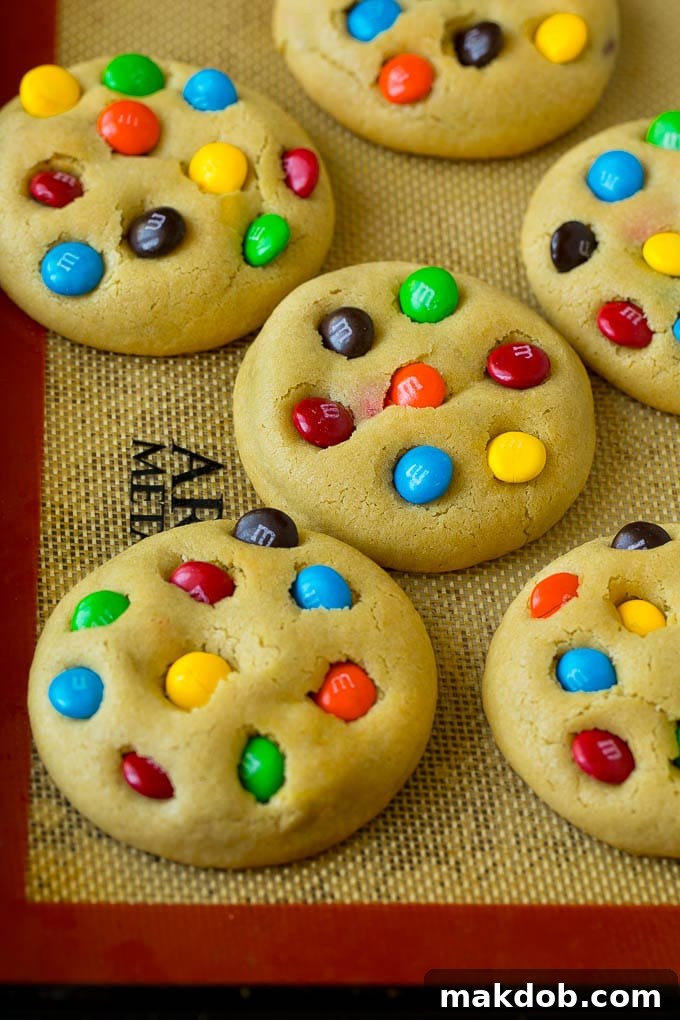 Freshly baked M&M cookies resting on a sheet pan, showcasing their golden-brown edges and soft centers filled with colorful chocolate candies.
