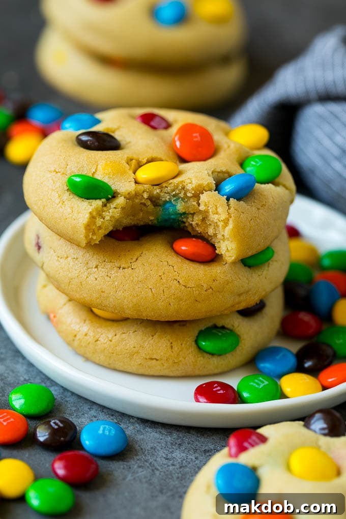 A stack of golden-brown M&M cookies, with a tempting bite taken out of the top one, revealing its soft interior and colorful chocolate candies.