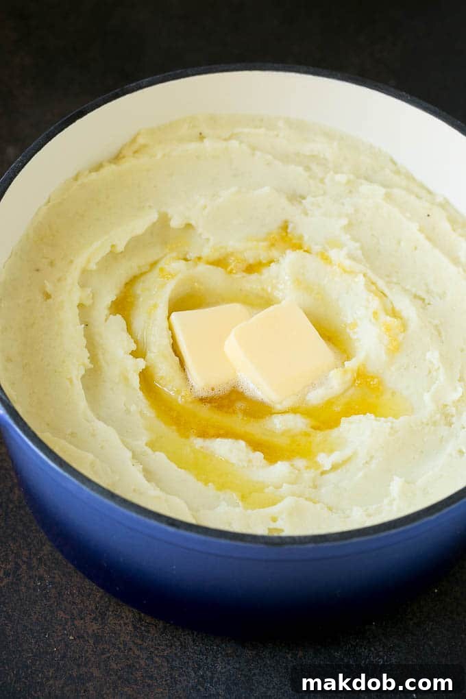 Garlic Mashed Potatoes Recipe #garlic #potatoes #mashedpotatoes #sidedish #dinner #thanksgiving #dinneratthezoo Creamy garlic mashed potatoes served in a bowl, topped with melting pats of butter and a sprinkle of fresh herbs.