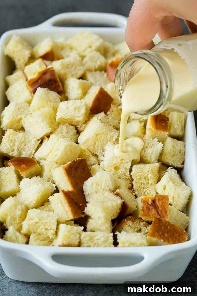 The sweet egg and milk custard mixture being poured over the challah bread cubes in a baking dish.