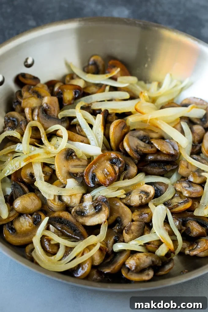 Sautéed mushrooms and onions simmering in a skillet, forming the gravy base.