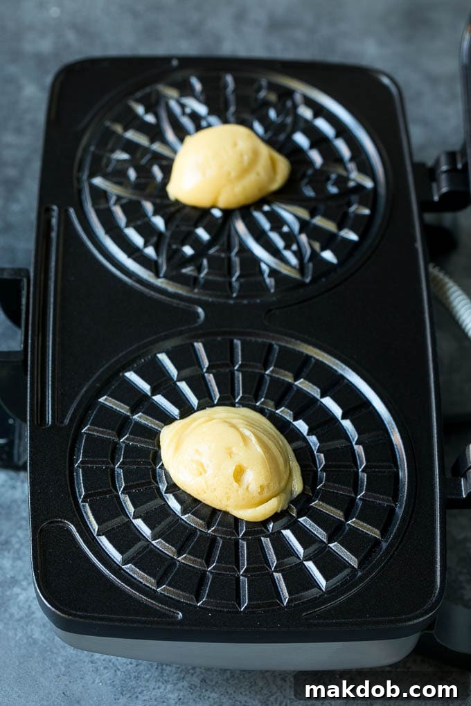 Small dollops of vanilla cookie batter carefully placed onto the patterned grids of a pizzelle iron.