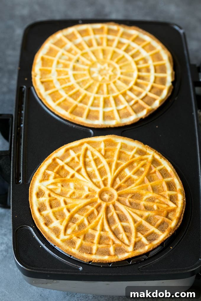 Baked pizzelle cookies inside a heated pizzelle iron, showing their intricate patterned surface.