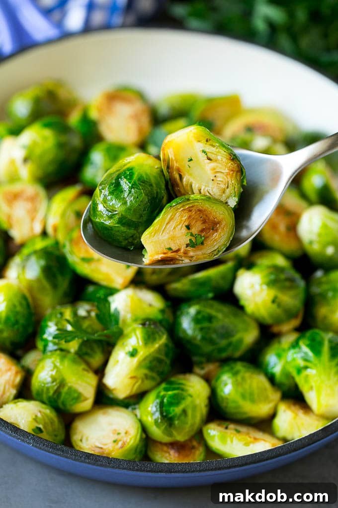 Sauteed Brussels Sprouts Recipe | Brussels Sprouts Side Dish #brusselssprouts #sprouts #veggies #sidedish #garlic #vegetarian #dinner #dinneratthezoo A serving spoon lifting a portion of cooked brussels sprouts from a bowl, highlighting their tender interior and golden exterior.