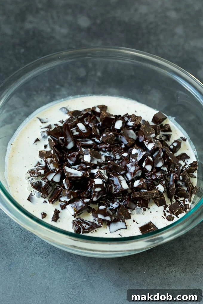 Hot heavy cream being poured over a pile of finely chopped chocolate in a glass bowl.