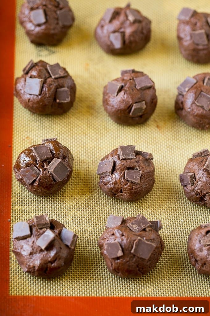 Perfectly formed balls of brownie cookie dough with additional chocolate pieces pressed into the tops, ready for baking.