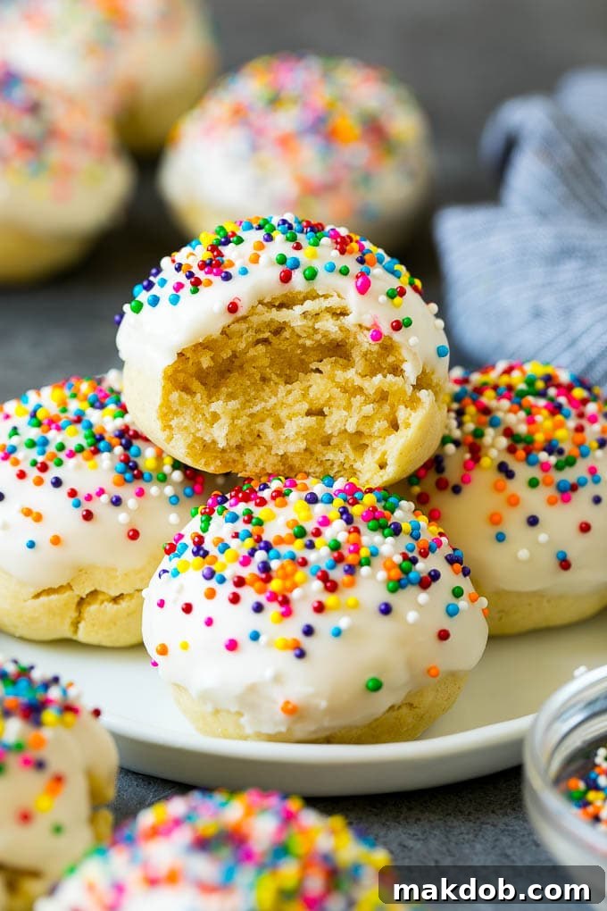 A plate of Italian cookies with a bite taken out of one, showcasing their soft texture and colorful sprinkles.