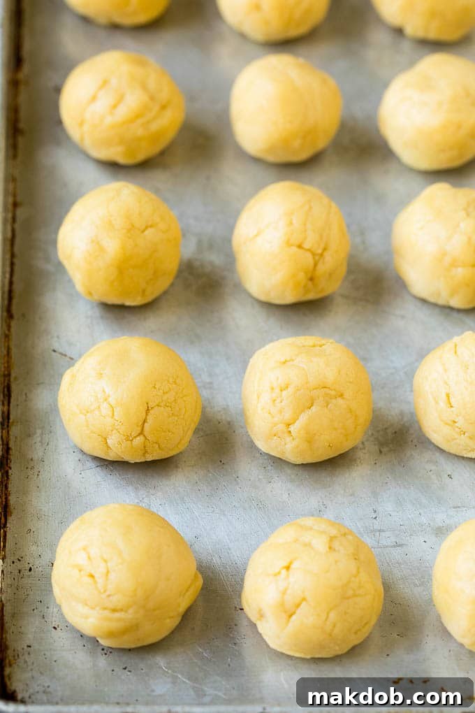 Balls of cookie dough neatly arranged on a sheet pan, ready for chilling and baking.