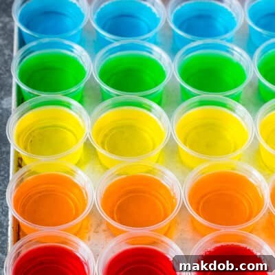 Ultimate Jello Shot Guide 6 Rows of rainbow colored Jello shots lined up on a sheet pan.