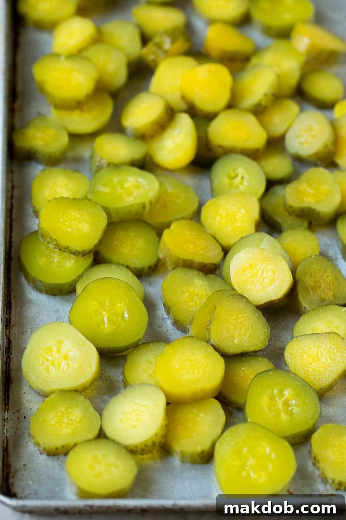 Perfectly sliced dill pickles, cut to an ideal 3/4 inch thickness, arranged neatly on a sheet pan, ready for the next steps in creating delicious fried pickles.