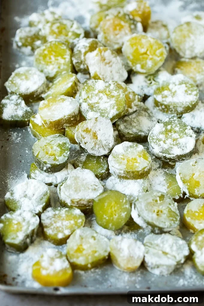 Dill pickle slices lightly coated in flour, a crucial preliminary step before dipping them into the beer batter to ensure maximum adhesion and crispiness.