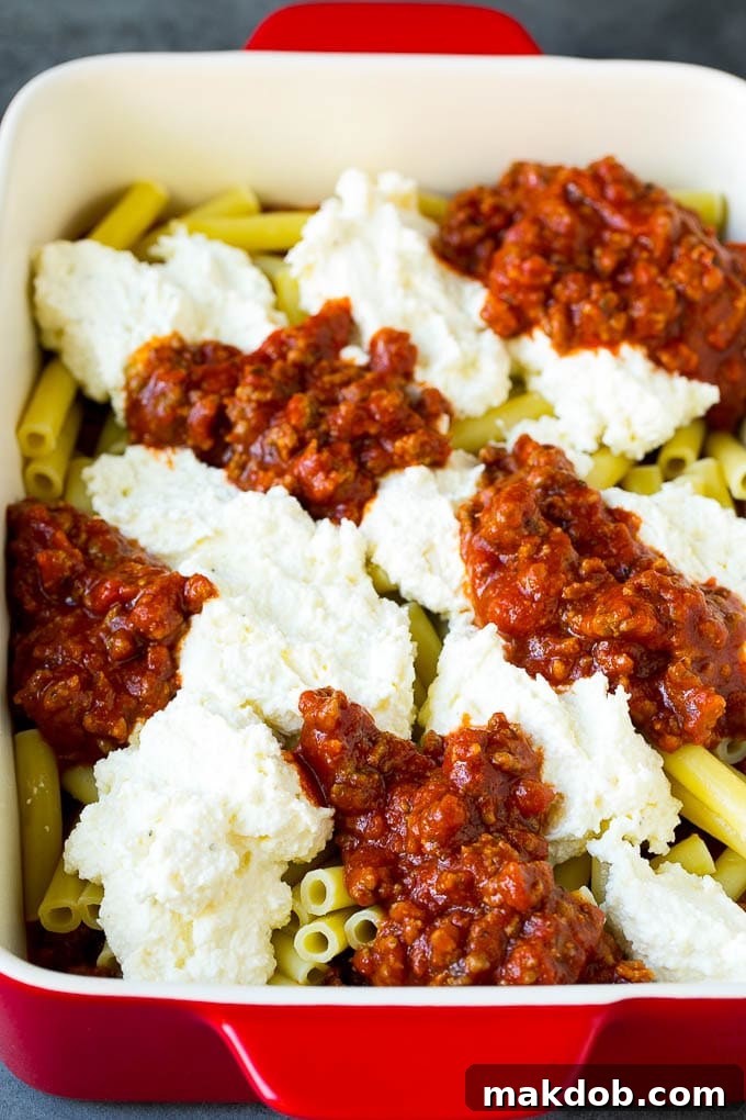 Cooked ziti pasta with dollops of meat sauce and ricotta cheese mixture, ready for layering.