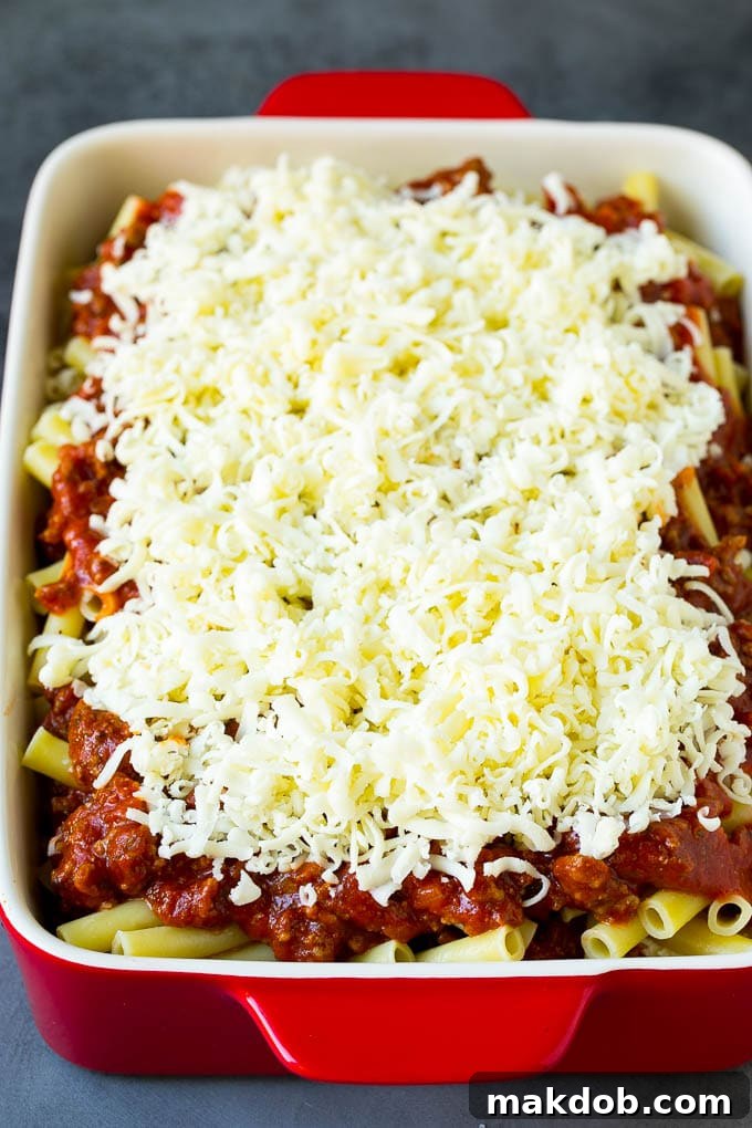 A baking dish filled with layered baked ziti, topped with shredded cheese before baking.