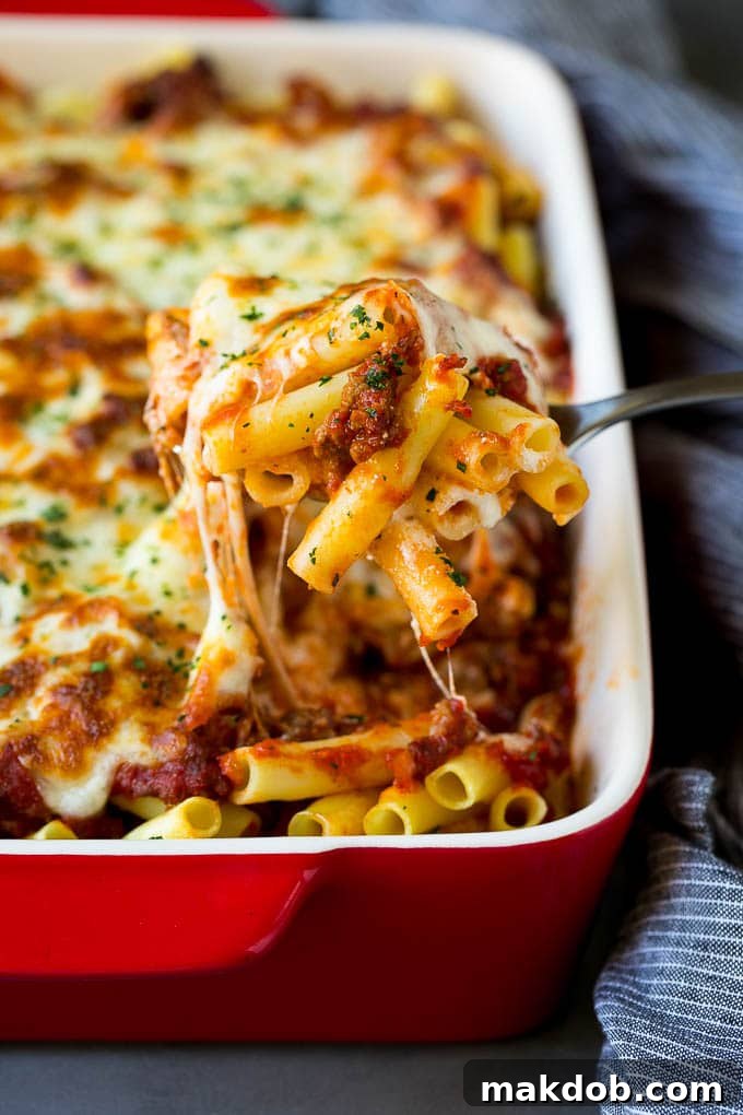 A spoon serving up a portion of baked ziti pasta, showing the layers of cheese and sauce.