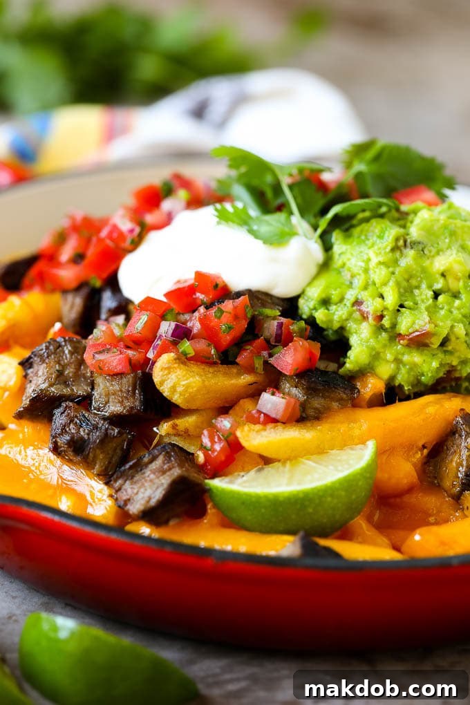Carne asada fries in a skillet topped with sour cream, pico de gallo and steak, ready to be devoured.