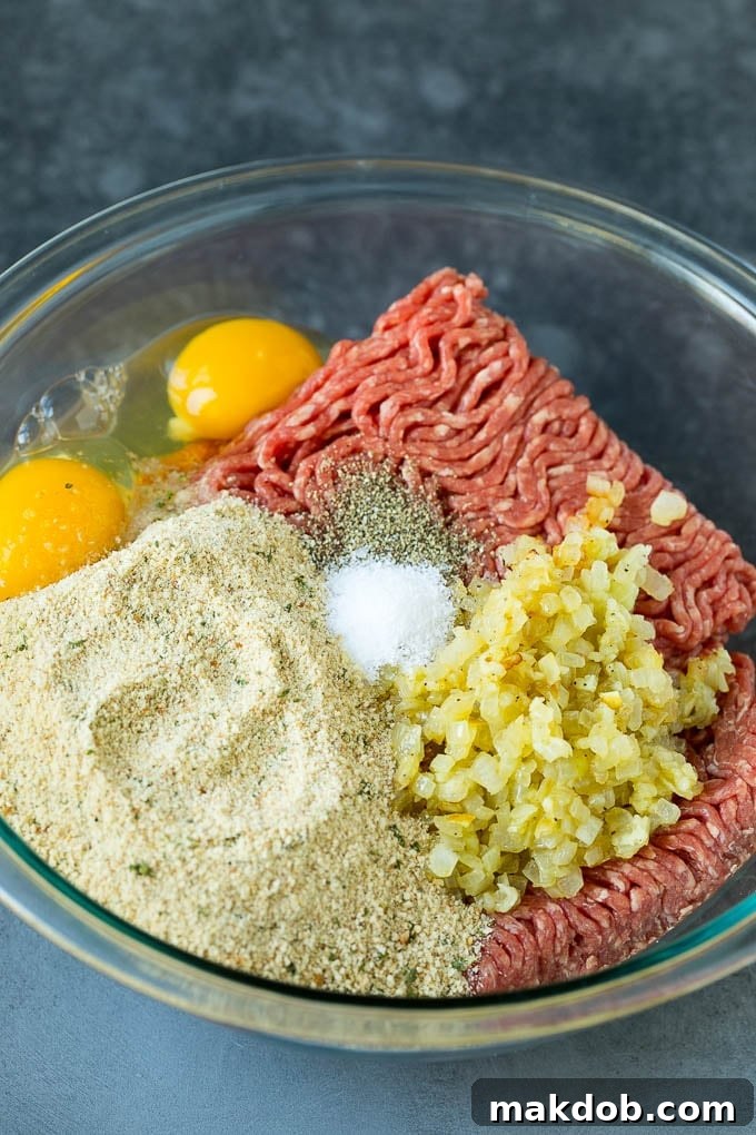 Ground beef, breadcrumbs, eggs, onion and seasonings in a bowl, ready to be mixed.