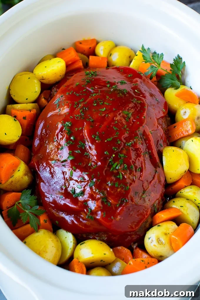 Crockpot meatloaf topped with ketchup and surrounded by carrots and potatoes, ready to be served.