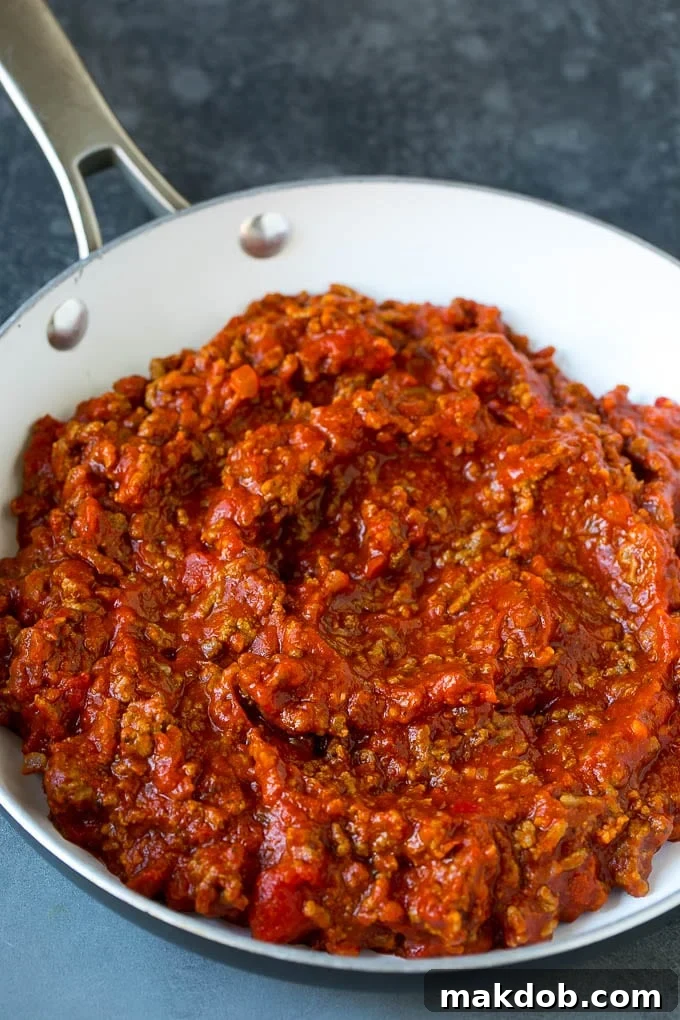 Rich meat sauce simmering in a pan, ready for lasagna roll ups.