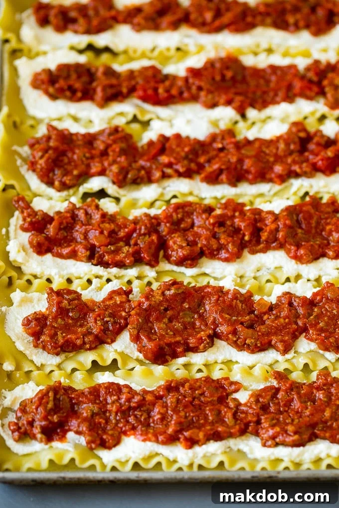 Lasagna noodles topped with creamy ricotta and savory meat sauce, ready for rolling.