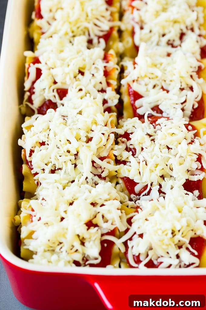 Lasagna noodles rolled up neatly in a baking dish, topped with sauce and melted cheese, ready for baking.