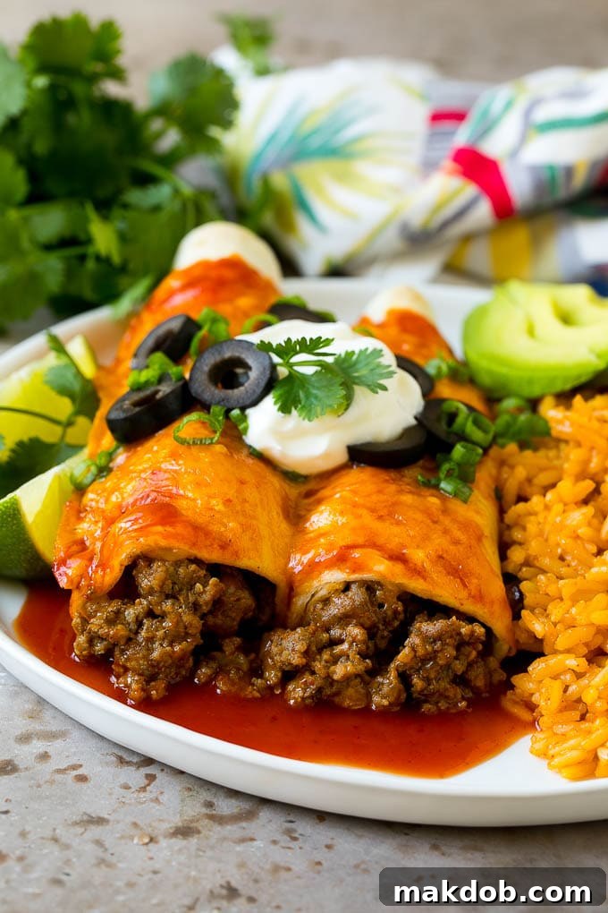 Ultimate Beef Enchiladas 2 A plate of beef enchiladas topped with sour cream, olives and green onions, ready to be served.