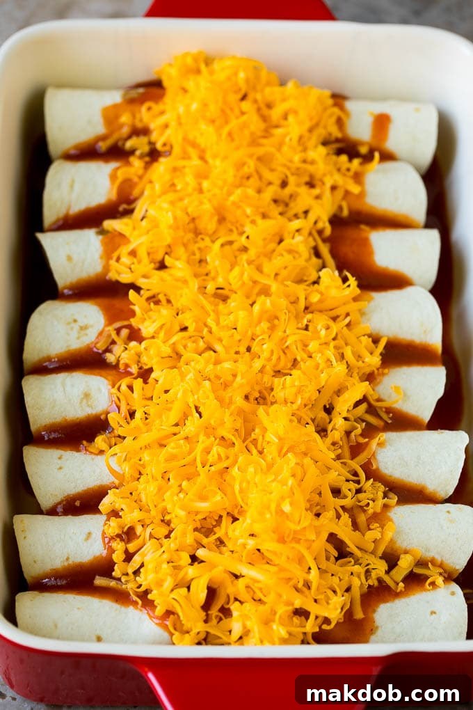 Ultimate Beef Enchiladas 5 Rolled flour tortillas filled with beef and topped with sauce and cheese, ready for the oven.